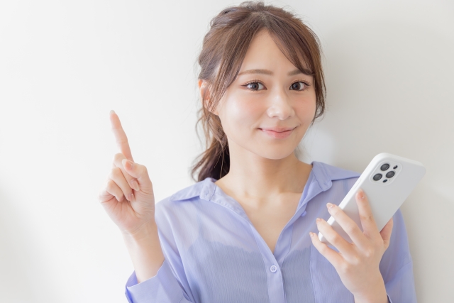 スマホを持って人差し指を立てる若い女性